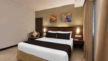 Ein Hotelzimmer mit einem großen Bett, zwei Nachttischlampen, einem Sessel und zwei an der Wand hängenden Bildern.