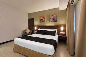 Una habitación de hotel con una cama grande, dos lámparas de noche, una silla y dos cuadros colgados en la pared.