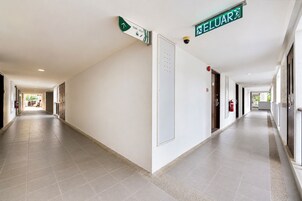 A long, well-lit corridor with directional signs, fire extinguishers, and doors on both sides.