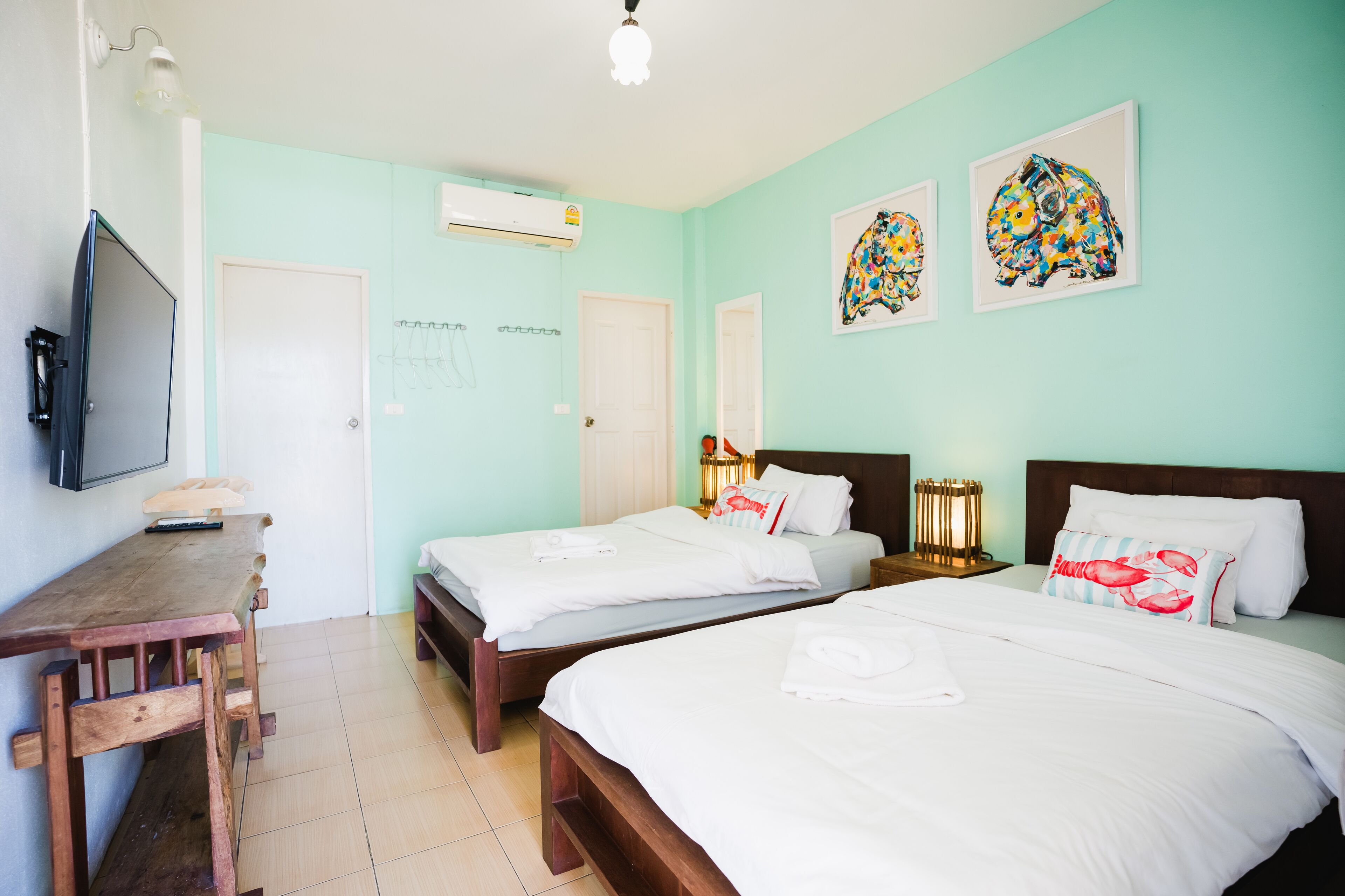 A hotel room with two beds, a desk, a TV, and artwork on the walls.