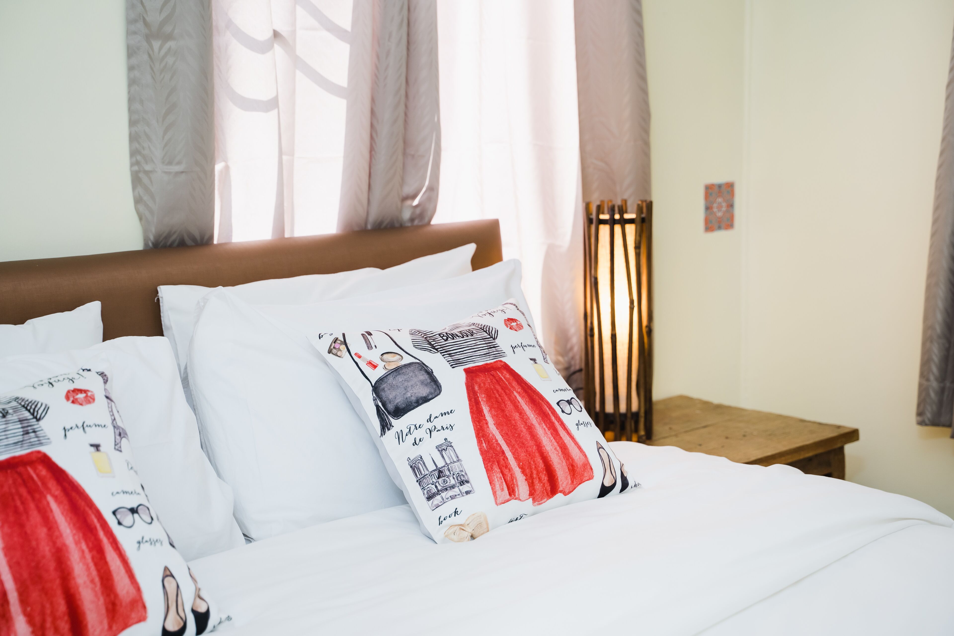 Un lit avec une literie blanche et des coussins décoratifs ornés d’illustrations de mode.