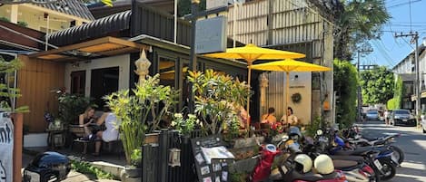 Un restaurante a la calle con mesas al aire libre, sombrillas amarillas y motocicletas estacionadas.