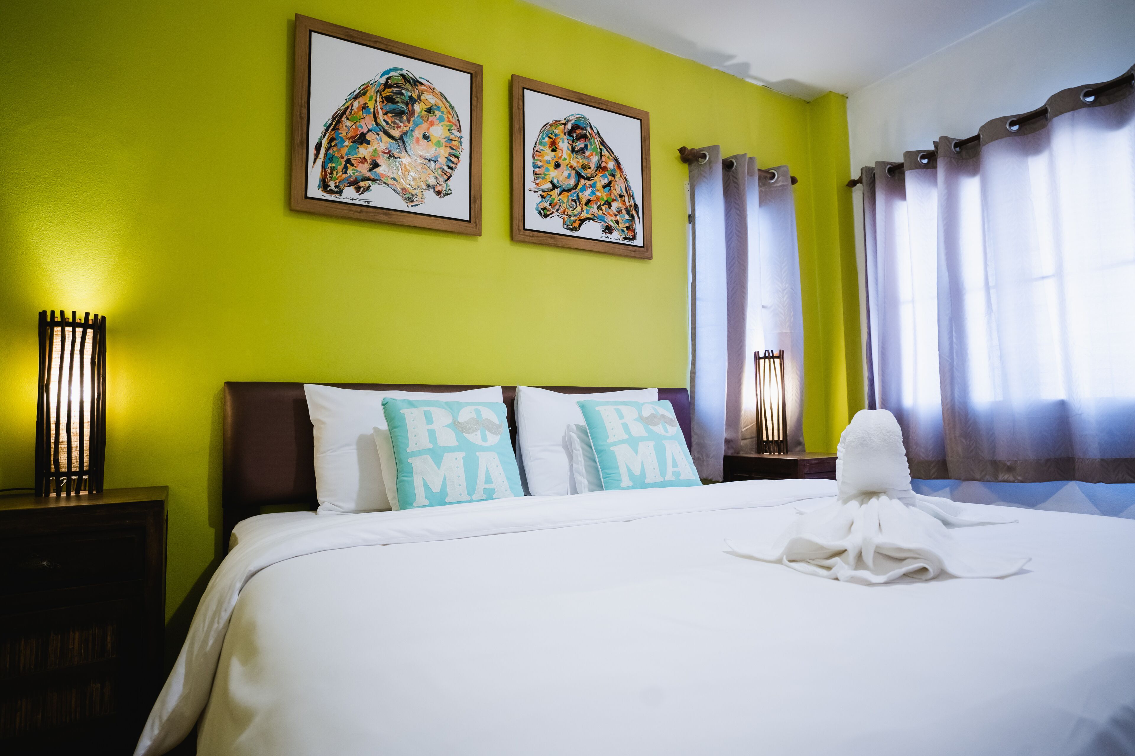 Una habitación de hotel con una cama, dos almohadas con el texto 'ROMS MAMA', dos cuadros enmarcados en la pared y una toalla sobre la cama.