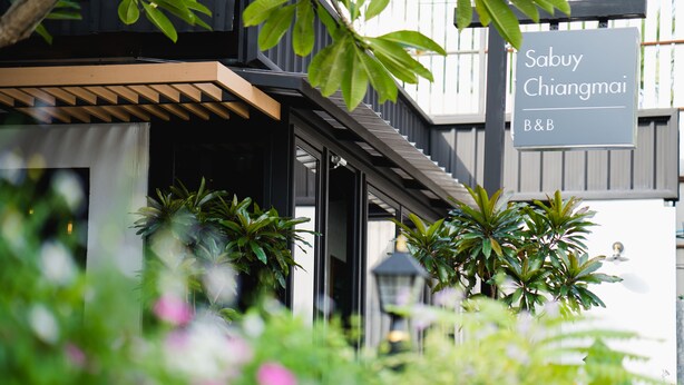 A building with a sign reading "Sabuy Chiangmai B&B" and a covered entrance area with plants.