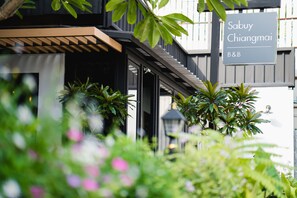 Un bâtiment avec une enseigne indiquant « Sabuy Chiangmai B&B » et une zone d’entrée abritée, agrémentée de plantes.