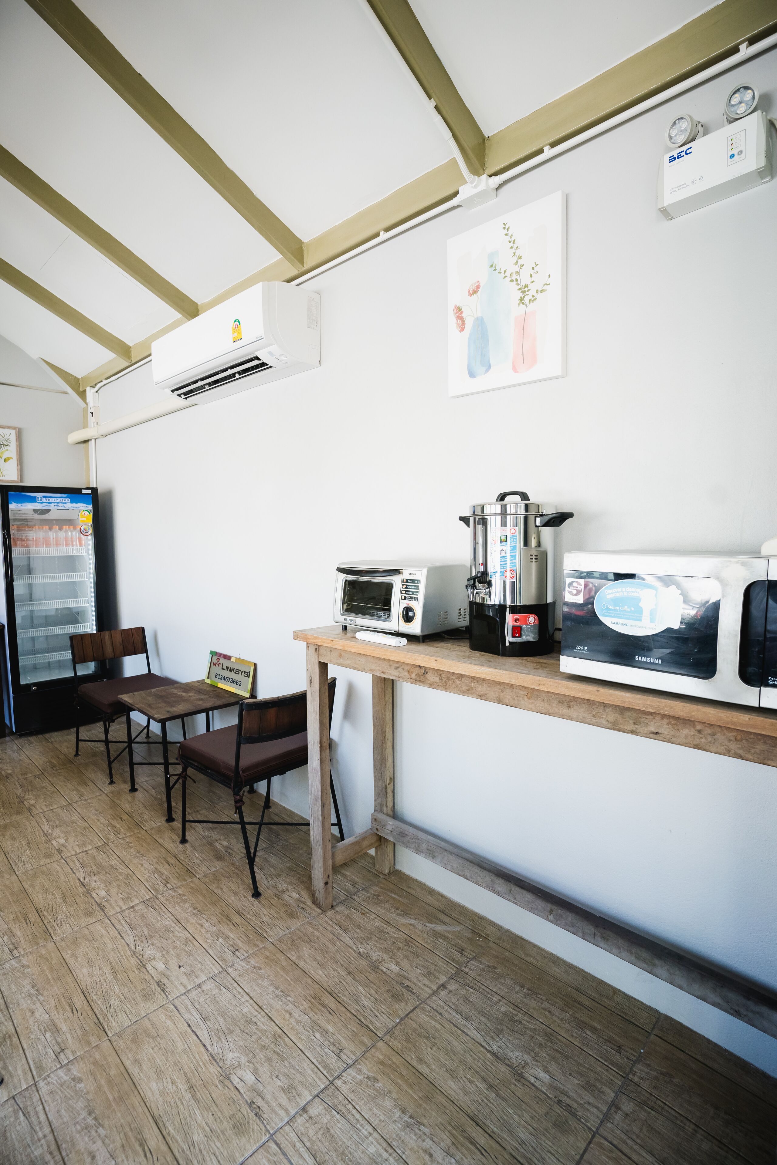 A kitchenette with a microwave, toaster, coffee maker, and a refrigerator. There are two chairs and a small table.