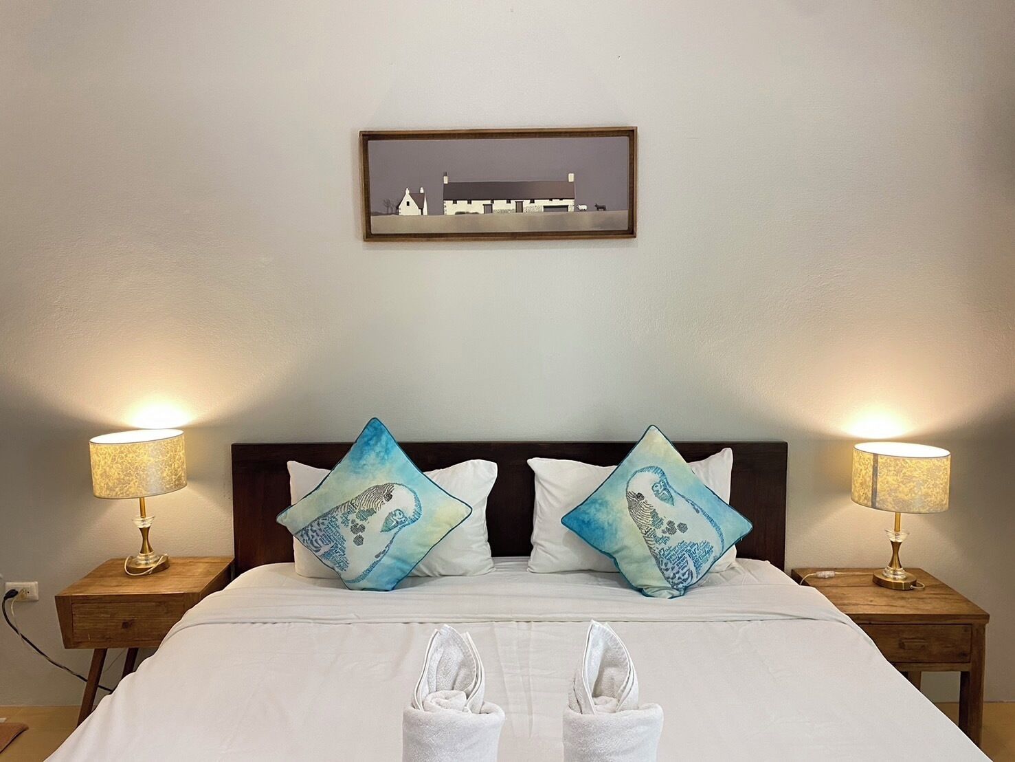 A neatly made bed with two pillows, two bedside lamps, and a framed picture on the wall.