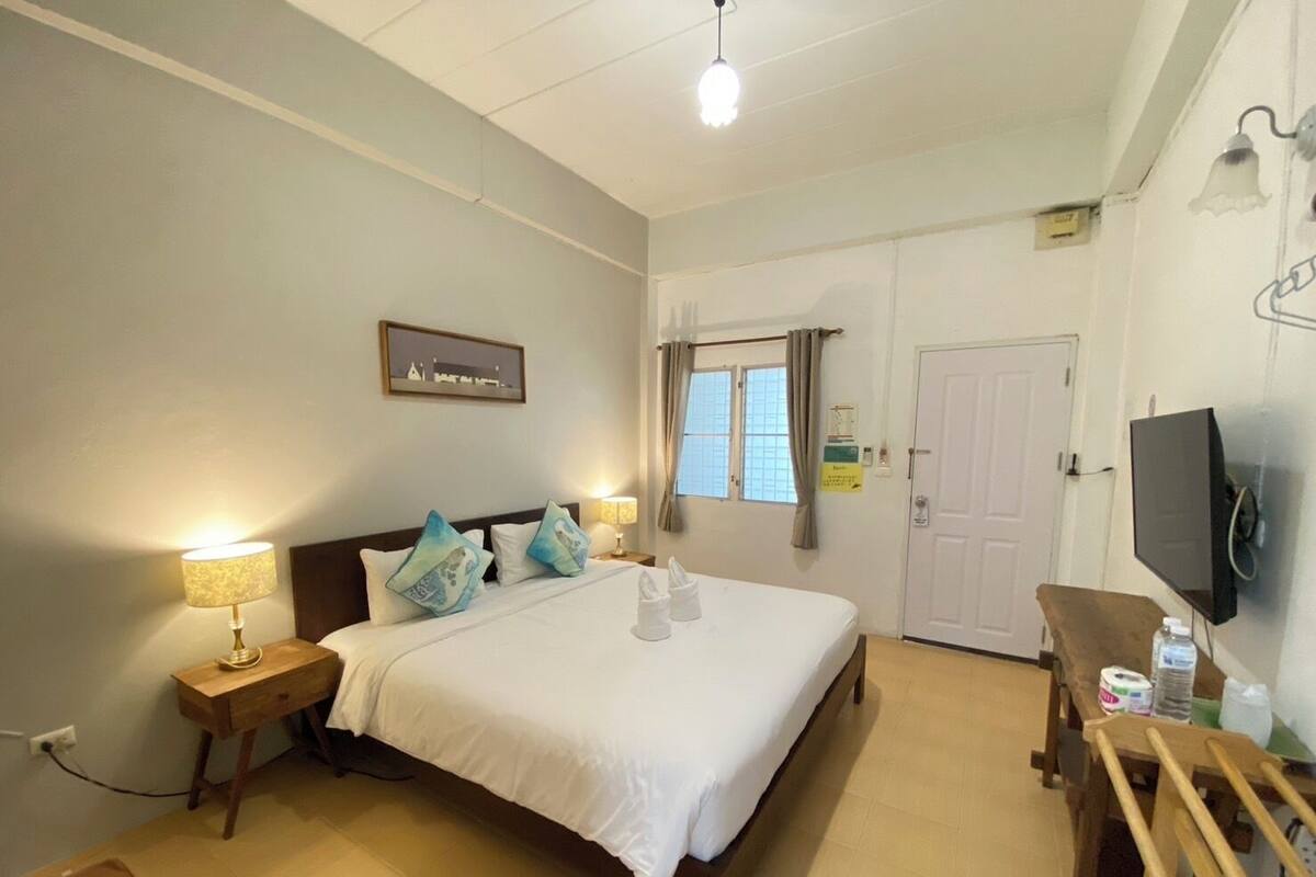 Une chambre d’hôtel comprenant un lit, des tables de chevet, un bureau, une chaise, une télévision et une fenêtre avec des rideaux.