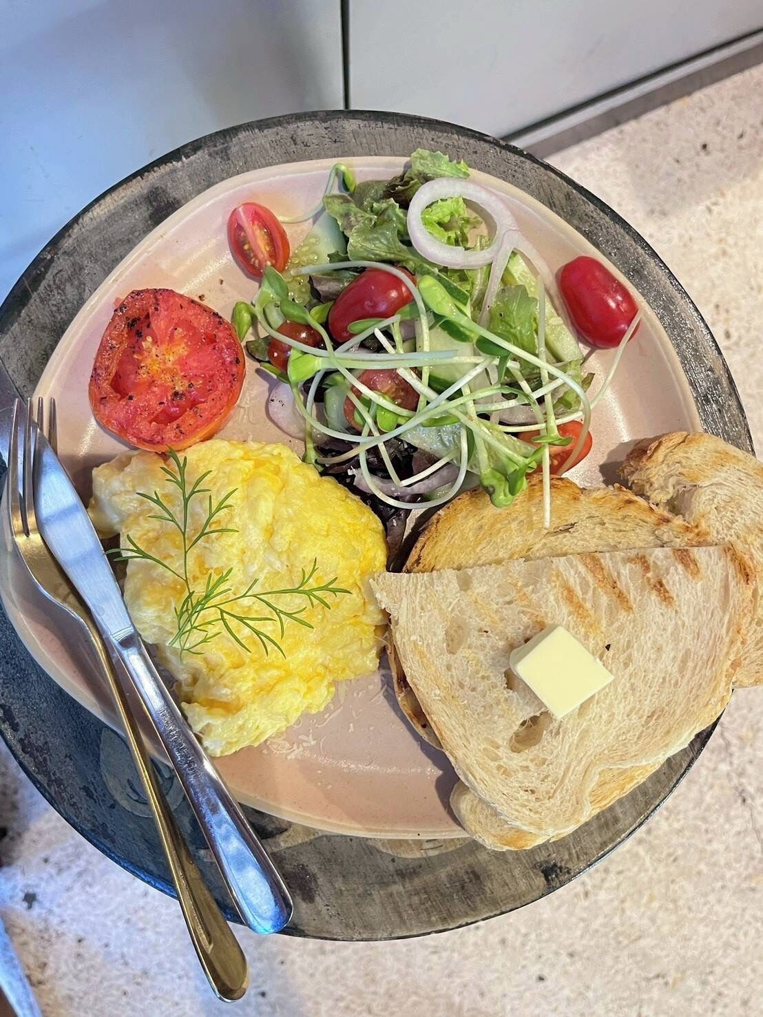 A plate with scrambled eggs, a salad, a slice of tomato, and two pieces of bread with butter.