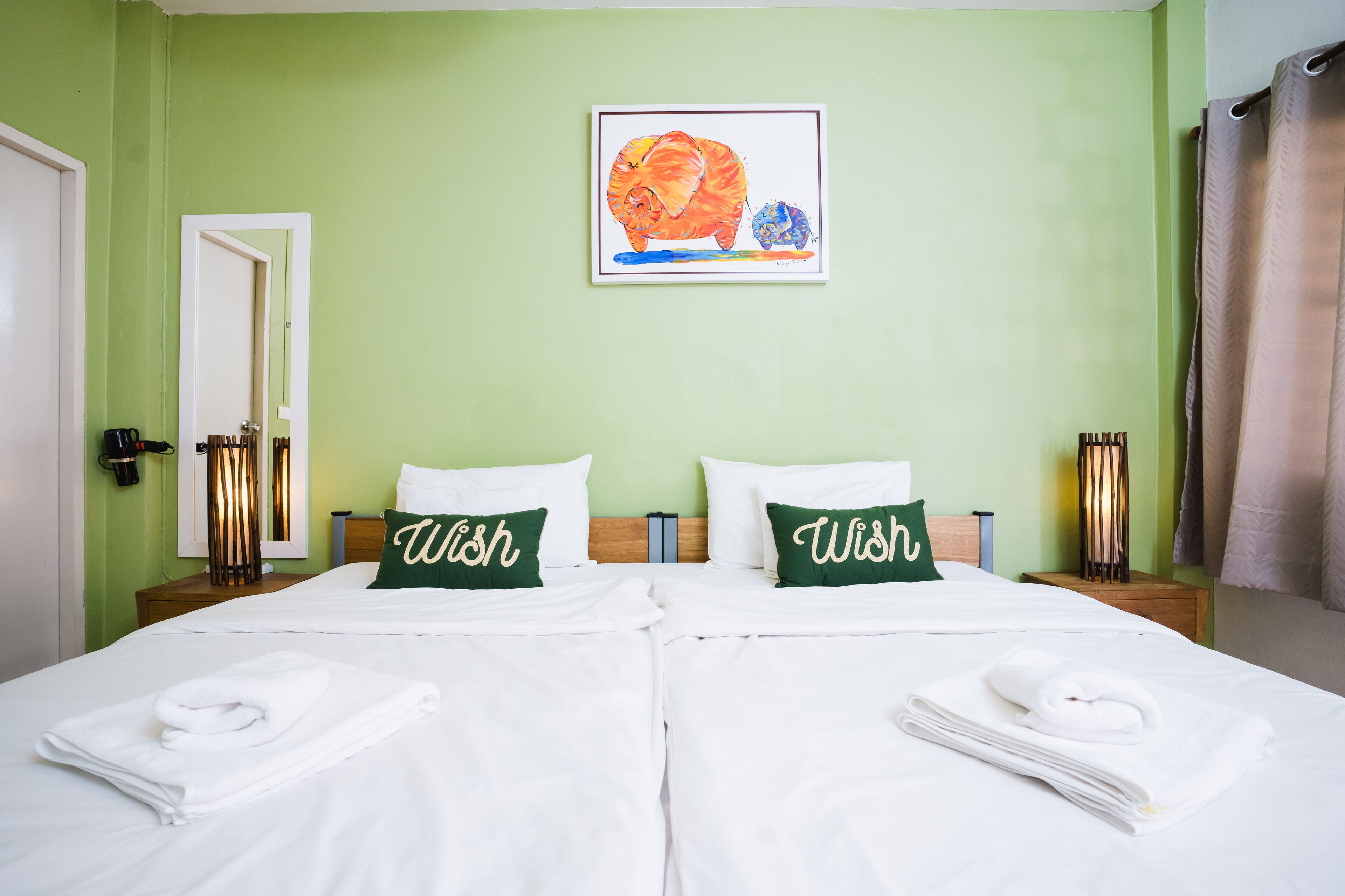 Habitación doble con dos camas, paredes verdes, un cuadro de un rinoceronte y almohadas con la palabra 'Wish'.
