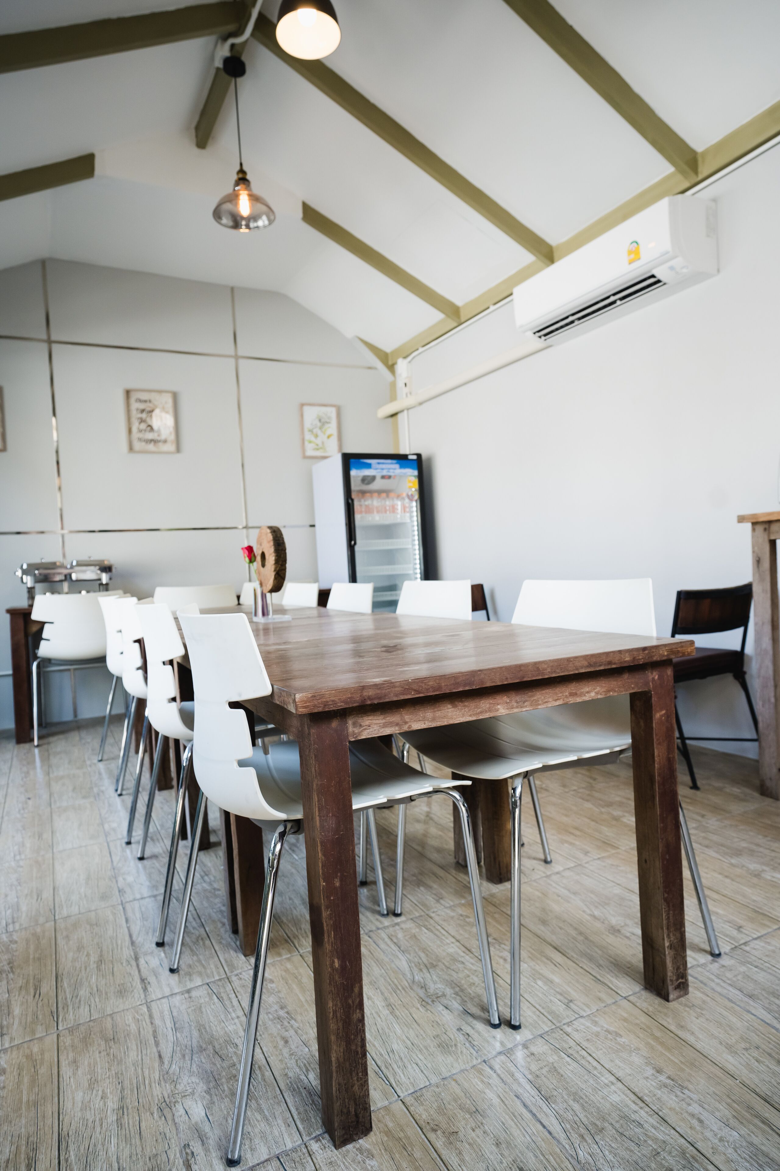 Un comedor con una mesa de madera y sillas blancas, una lámpara colgante y un equipo de aire acondicionado en la pared.