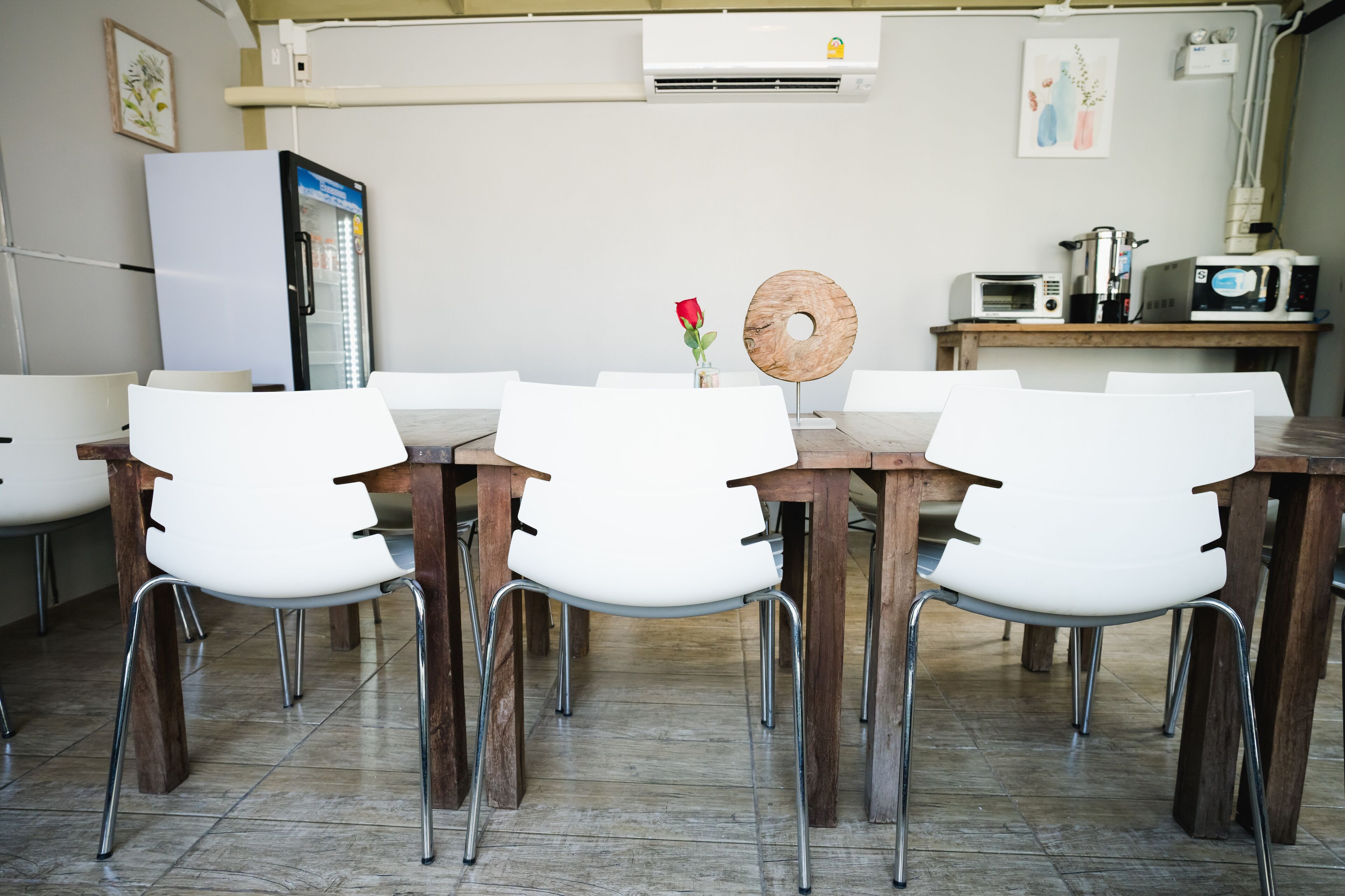 Un coin repas avec une table en bois et des chaises blanches, un réfrigérateur et un four à micro-ondes posés sur un comptoir en bois.
