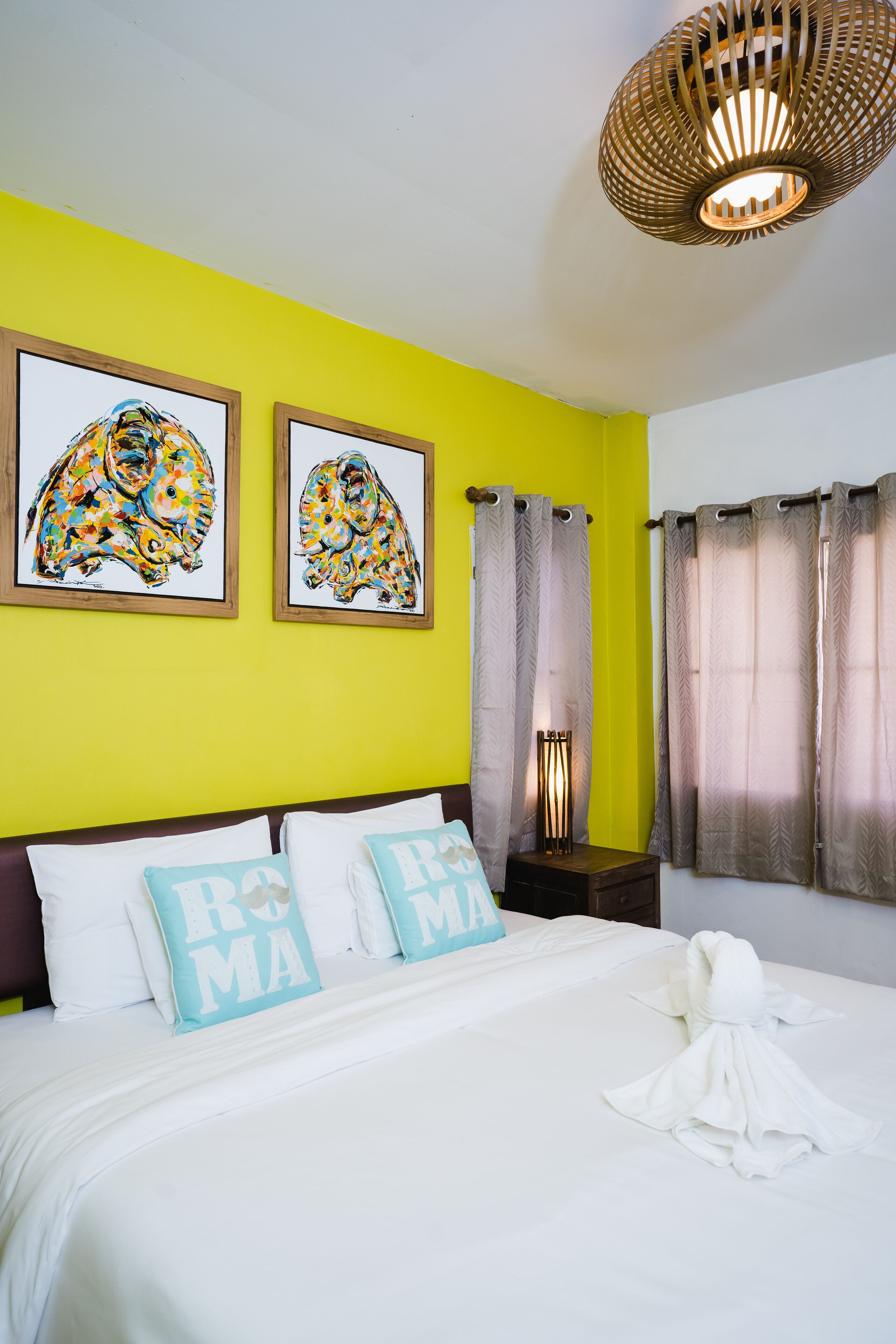 Habitación de hotel con cama, almohadas, una obra de arte en la pared, cortinas y una lámpara de techo original.