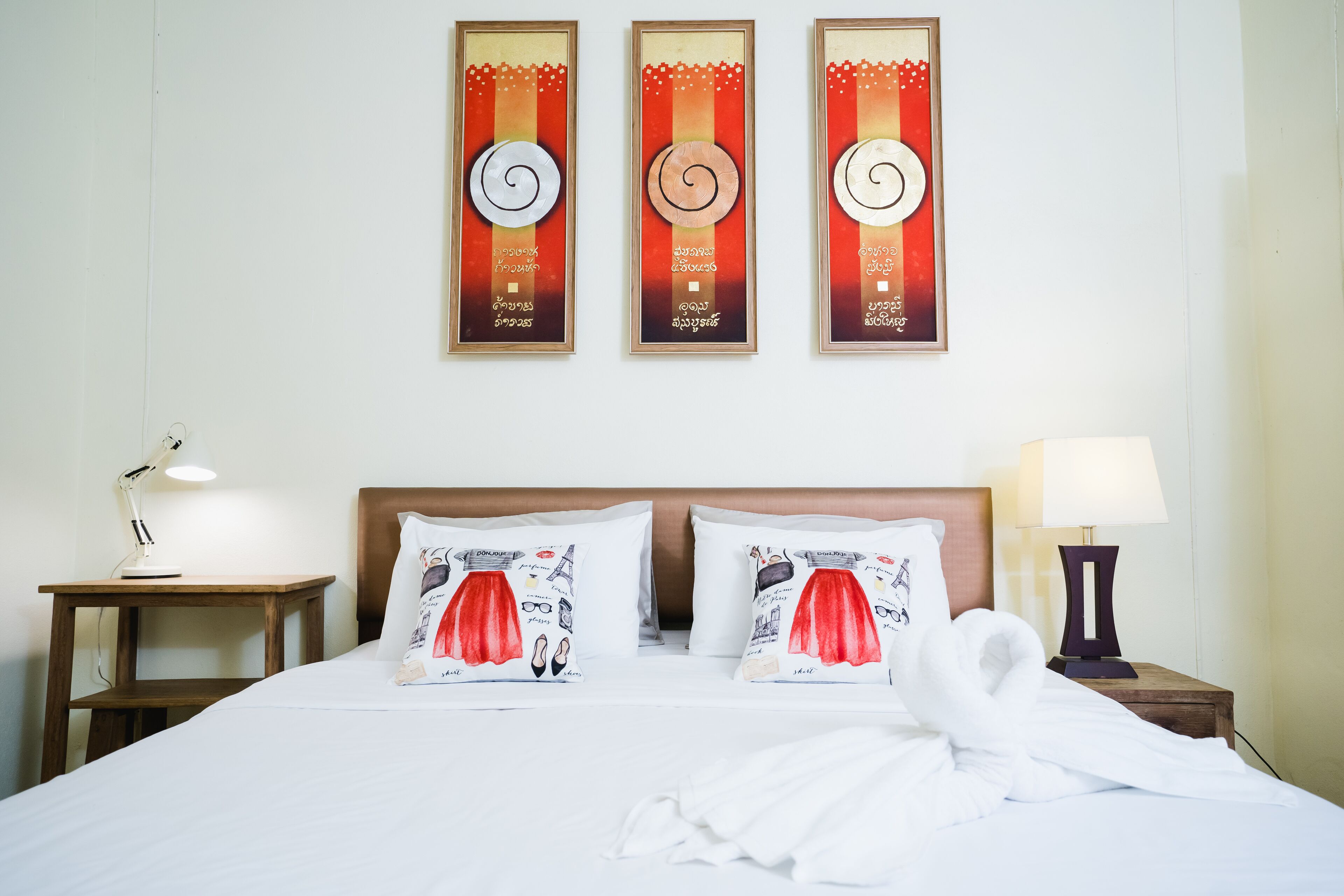 A hotel room with a neatly made bed, two bedside tables, and three wall-mounted artworks.