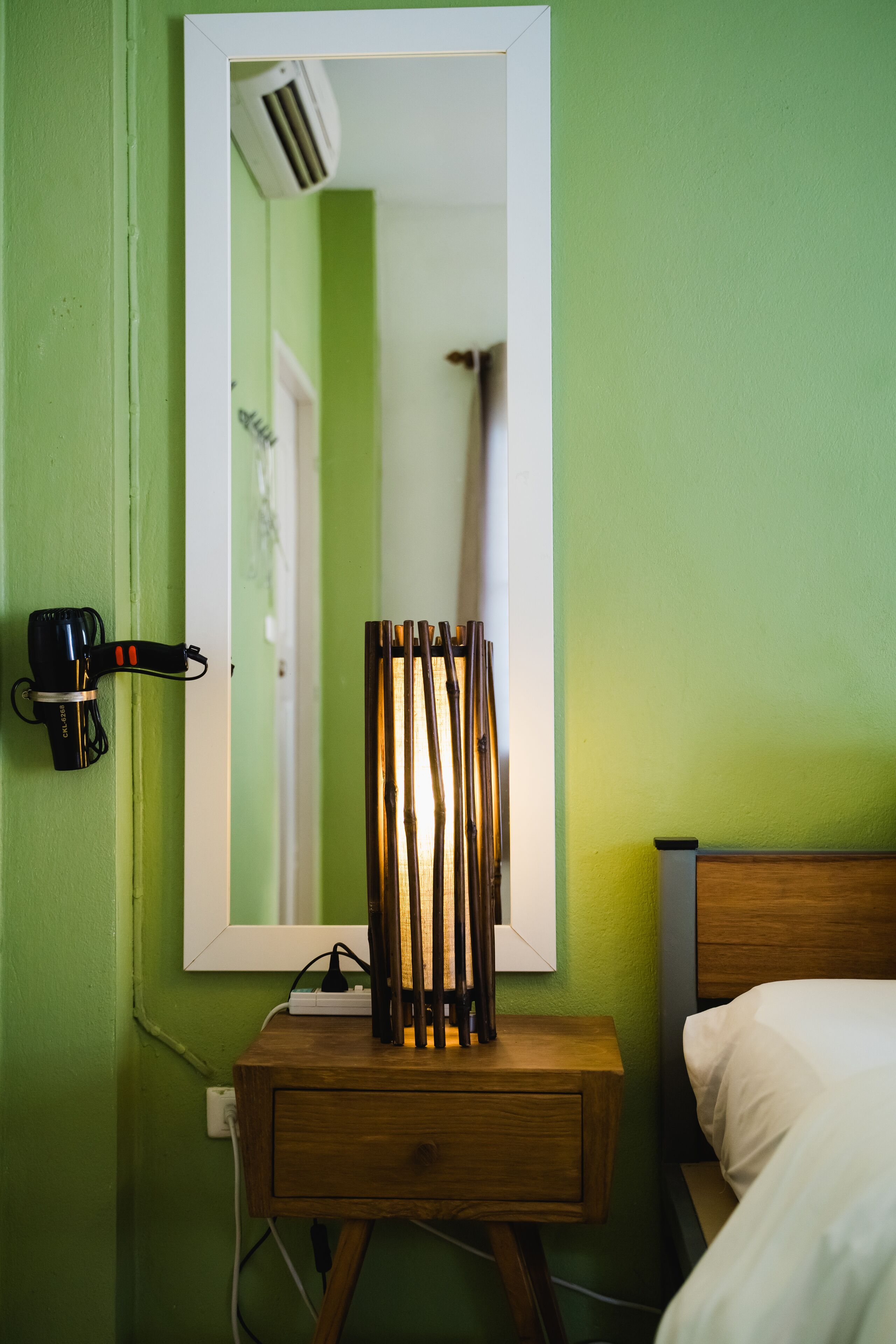 Et værelse med grøn væg, et trænatbord med lampe, et spejl og en seng.
