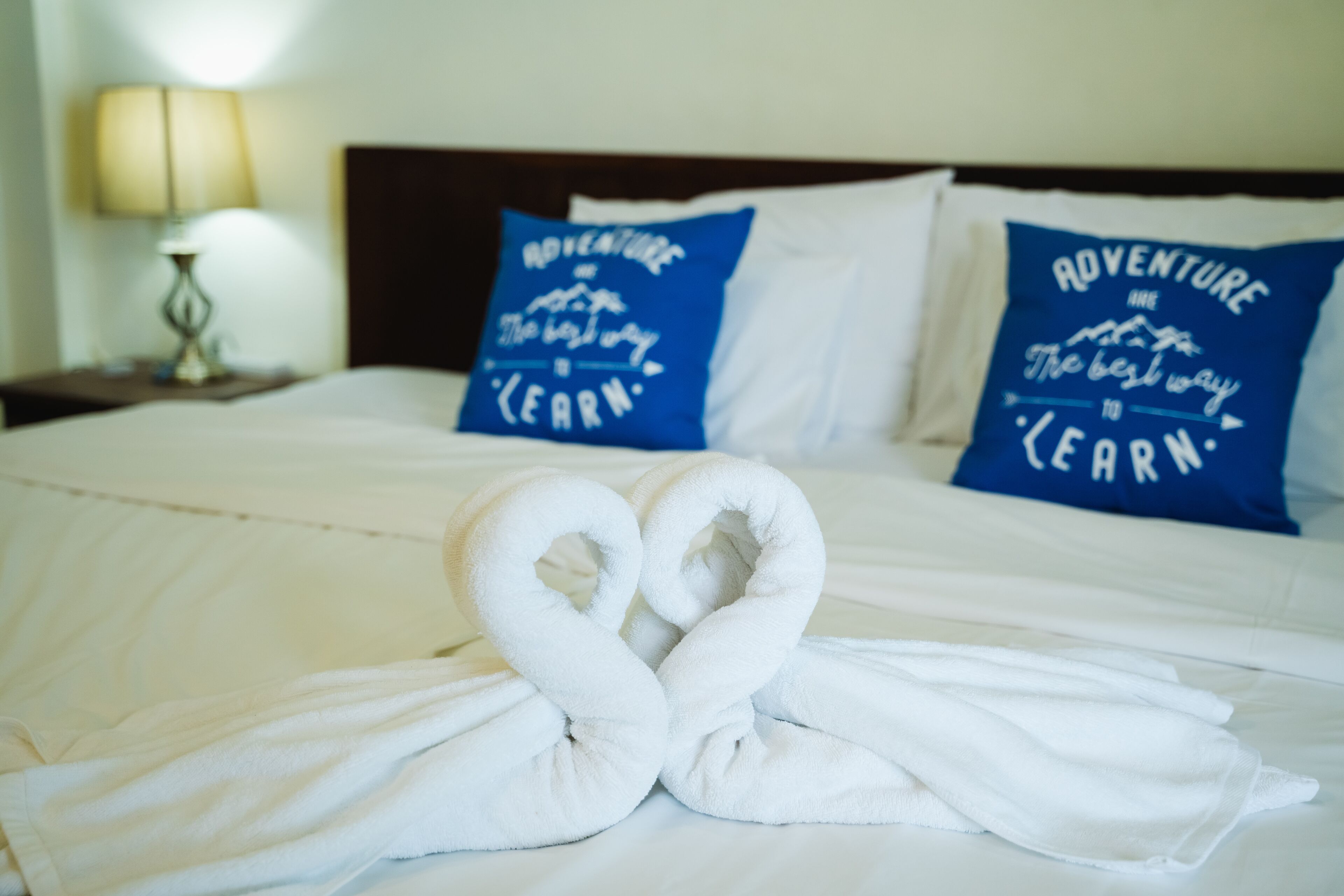 A neatly made bed with two pillows that read "Adventure is the best way to learn."
