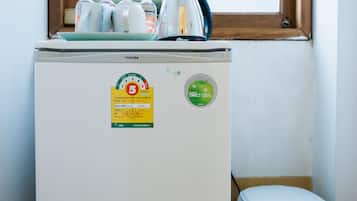 Un refrigerador compacto con dispensador de agua, cafetera y un cubo de basura en una esquina, sobre la cual hay una ventana.