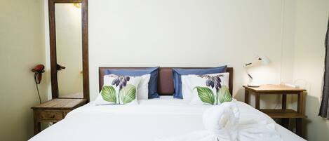 A neatly made bed with floral pillows, a wooden nightstand with a lamp, and a mirror on the wall.