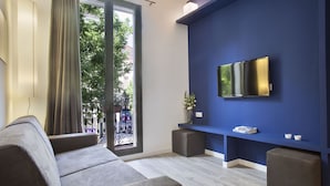 Uma sala de estar moderna com um sofá cinzento, uma televisão de tela plana presa a uma parede azul e uma varanda com vista para o verde.