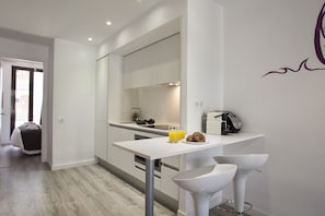 Une cuisine moderne avec des meubles blancs, un plan de travail blanc et un bar pour le petit-déjeuner avec deux tabourets. On y trouve un grille-pain et une machine à café sur le plan de travail.