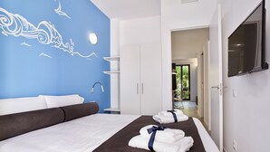 Quarto de hotel com uma cama grande, um mural azul na parede, uma TV e vista para o jardim.