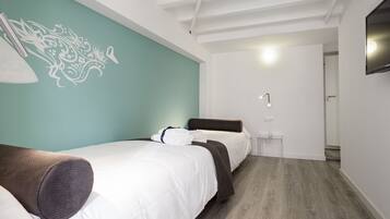 A modern hotel room with two beds, a teal accent wall, and a wooden floor.