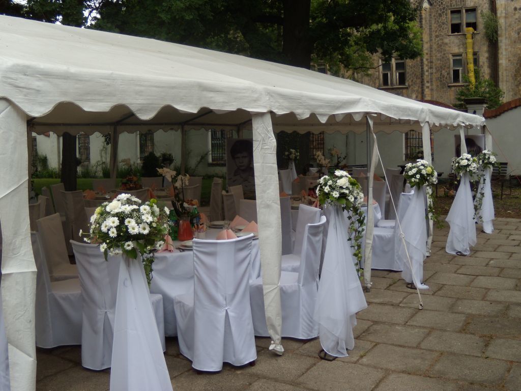 A tented outdoor event area with round tables and chairs, some with floral centerpieces.