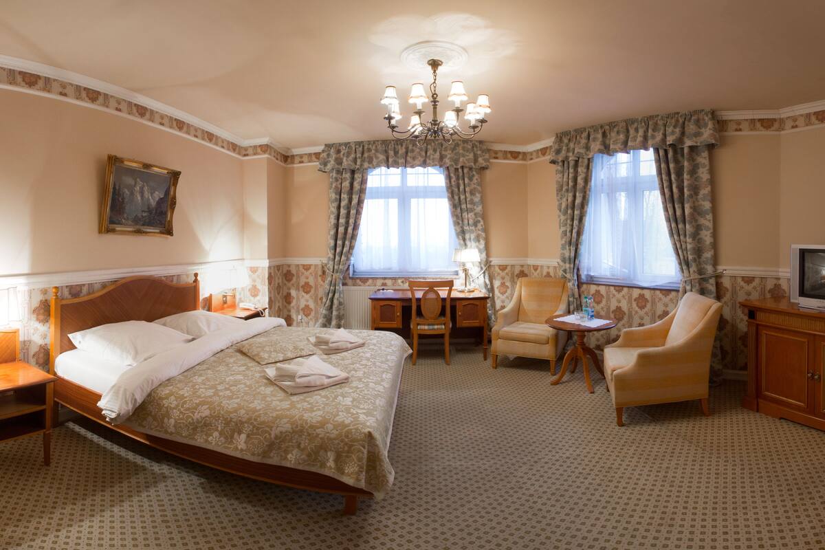 Ein Hotelzimmer mit einem Bett, einem Schreibtisch, zwei Sesseln, einem Fernseher und einer Chandelier.