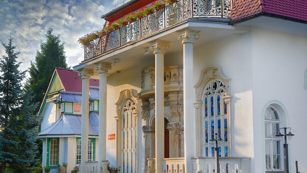 Een gebouw met een balkon, zuilen en een trap naar de ingang.