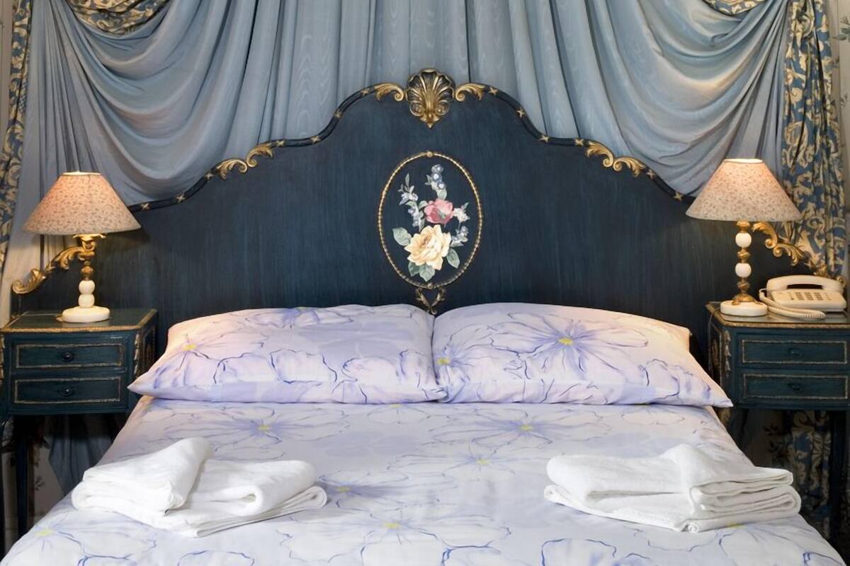 Ein Schlafzimmer mit einem großen Bett, einem aufwendigen Kopfteil, floralem Wandpapier und einer Chandelier.