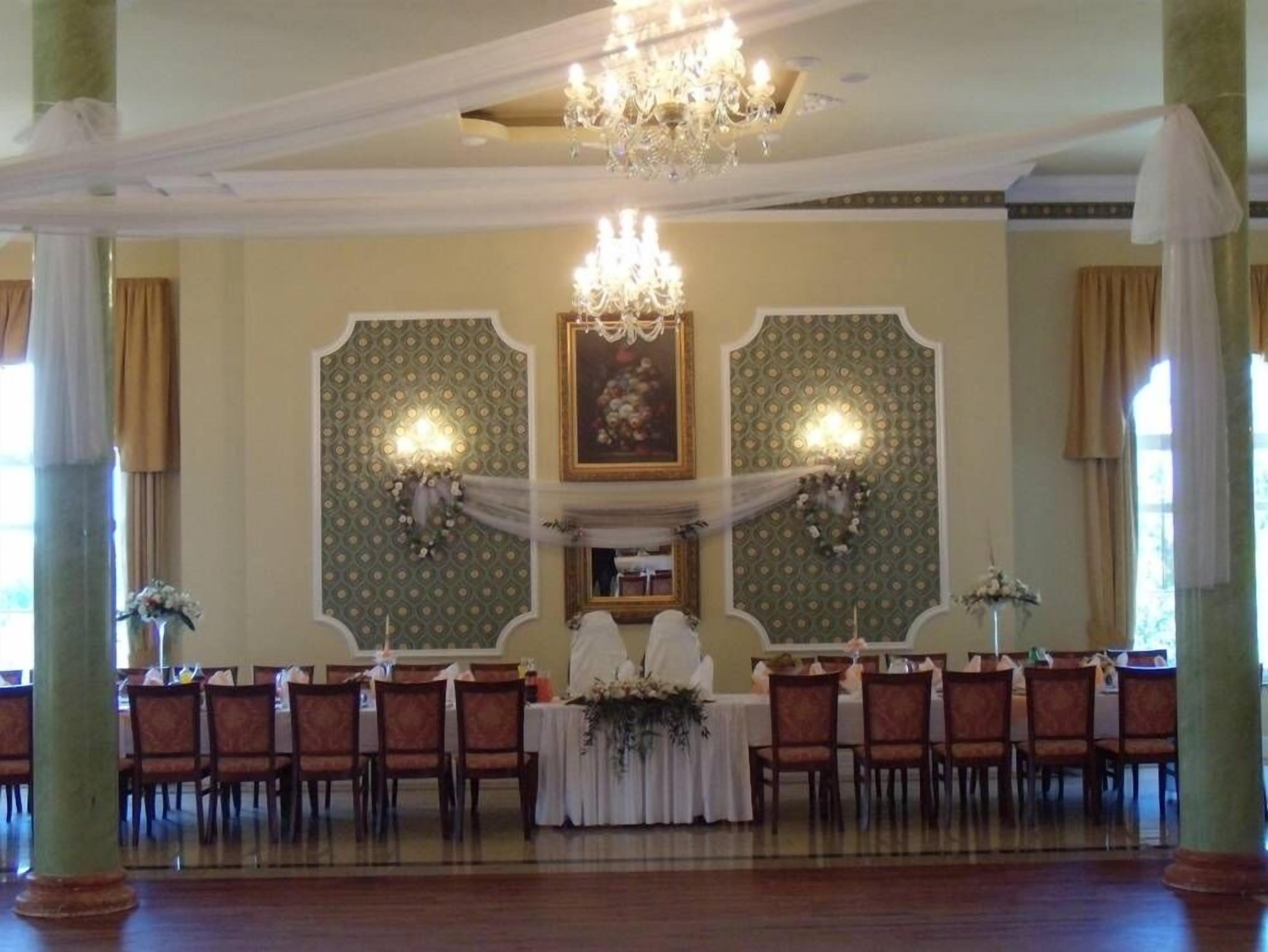 A banquet hall with a chandelier, patterned wallpaper, and a central table with floral arrangements.