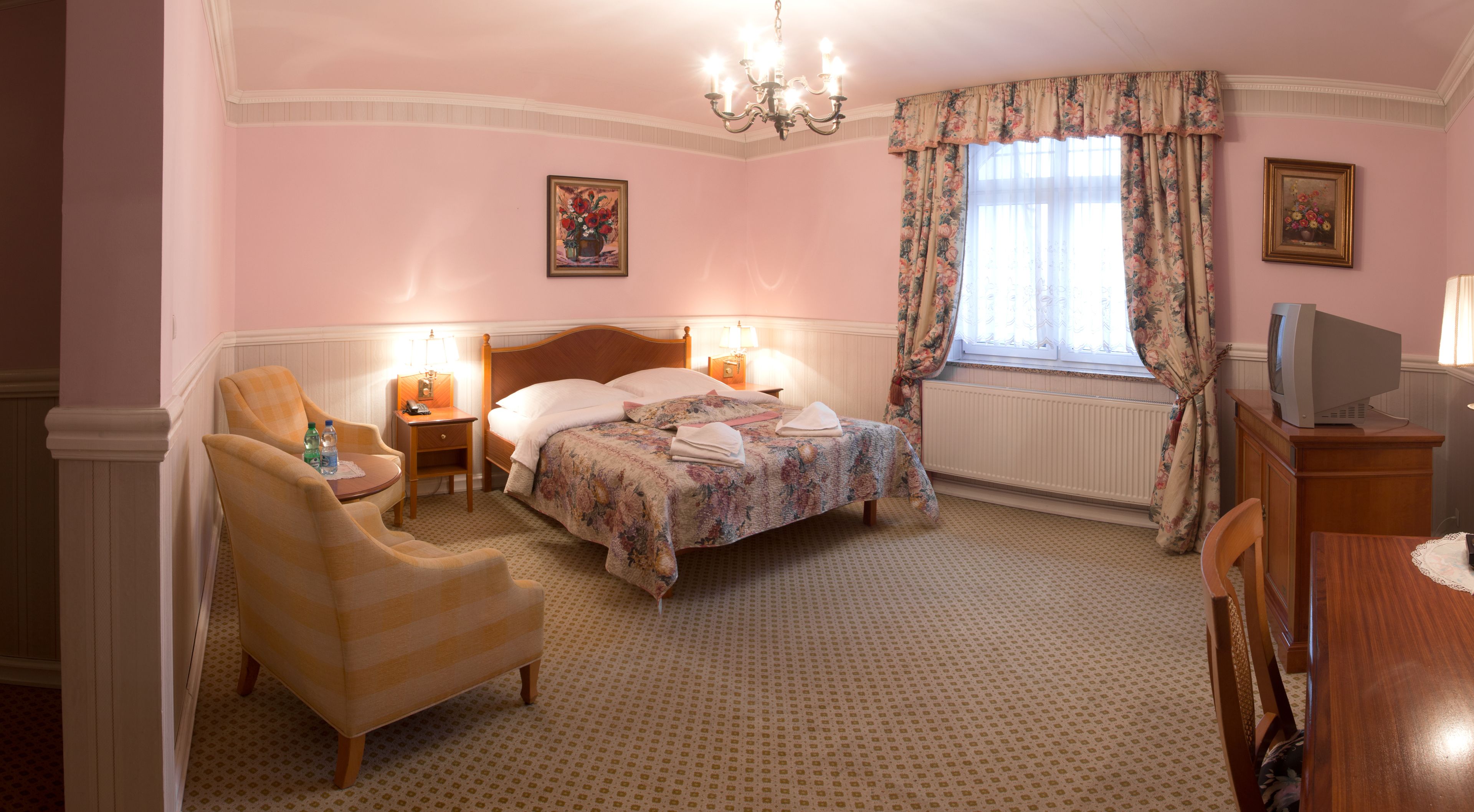 A hotel room with a bed, a chair, a desk, a television, and a window with curtains.