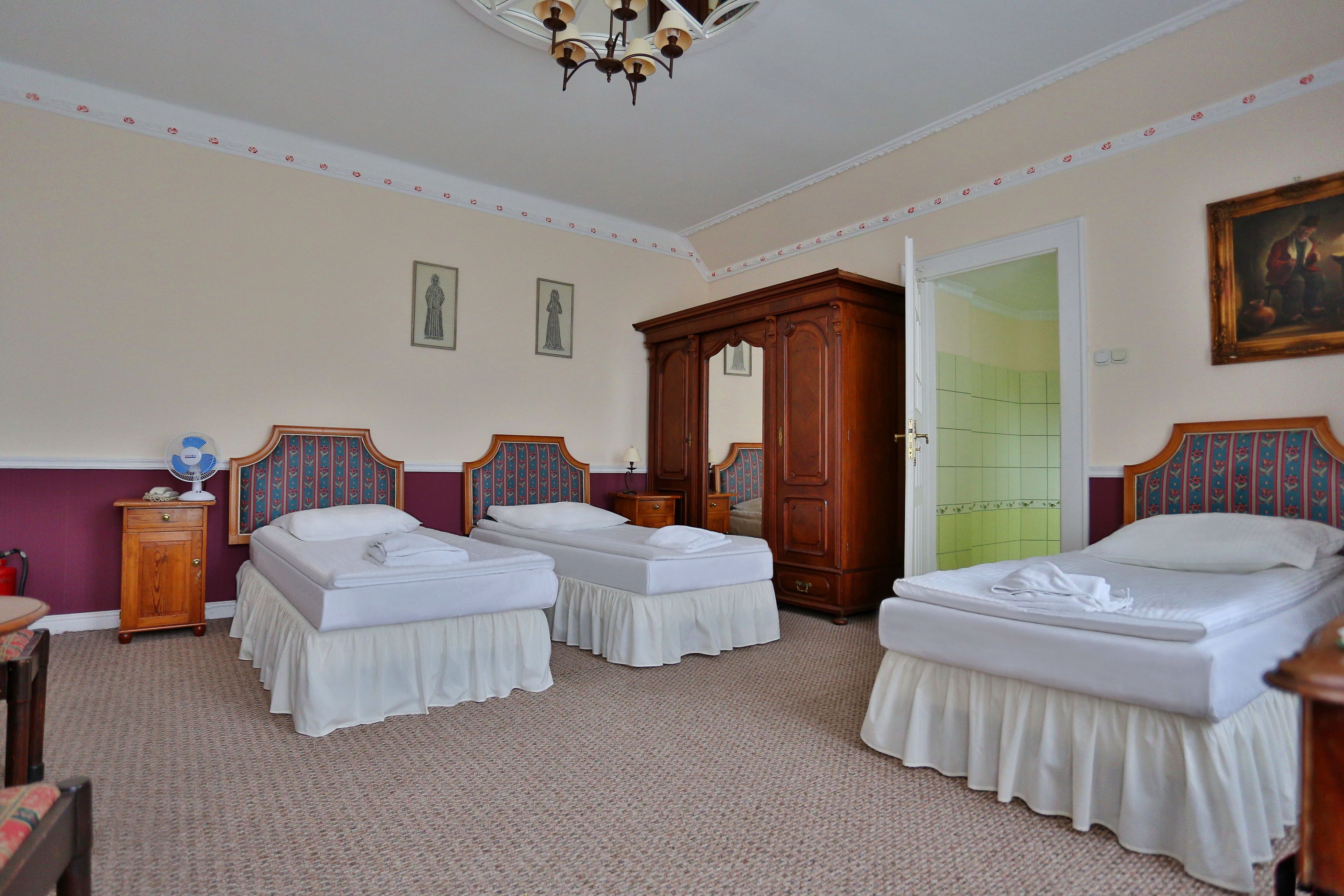 A hotel room with two single beds, a wooden wardrobe, a mirror, and a door leading to a bathroom.
