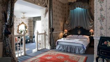 A bedroom with a large bed, ornate curtains, floral wallpaper, and a chandelier.