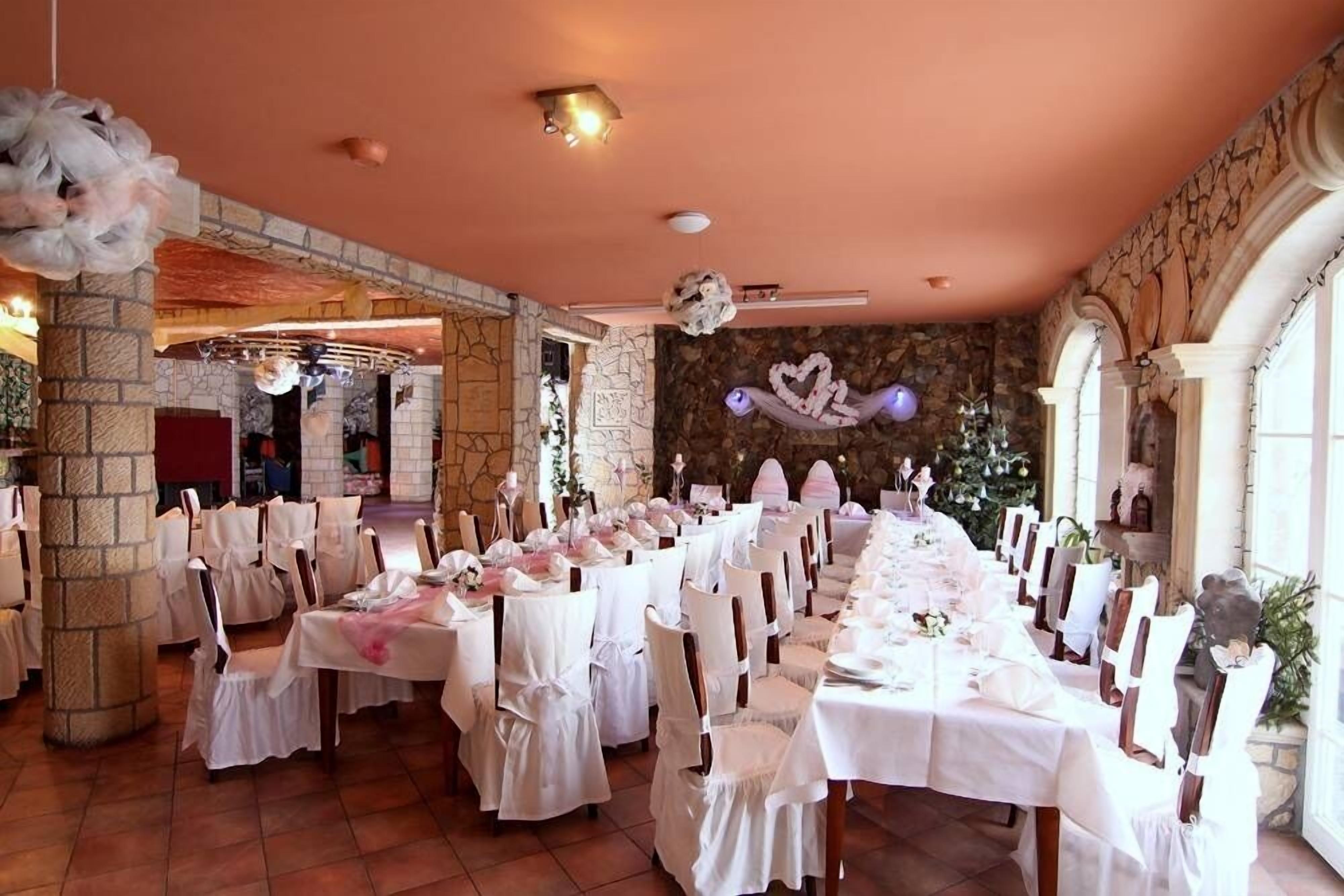 Une salle de banquet avec des nappes blanches, des chaises et un mur en pierre en arrière-plan.