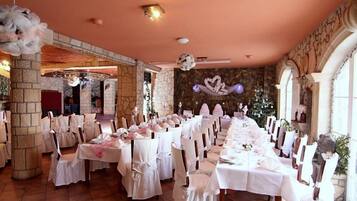 Une salle de banquet avec des nappes blanches, des chaises et un mur en pierre en arrière-plan.