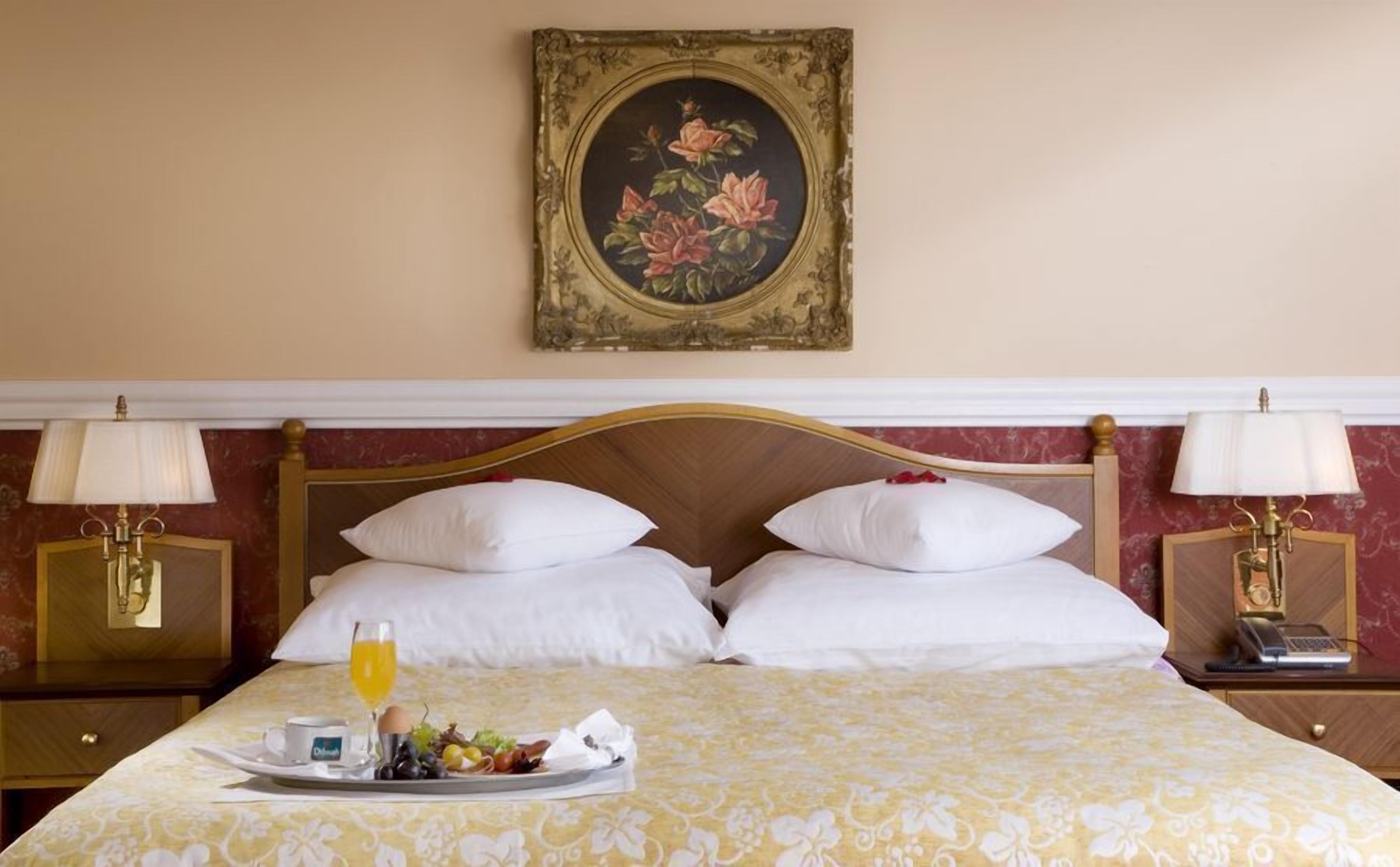 Une chambre d’hôtel avec un lit, deux tables de chevet, un plateau avec le petit-déjeuner et un tableau au mur.
