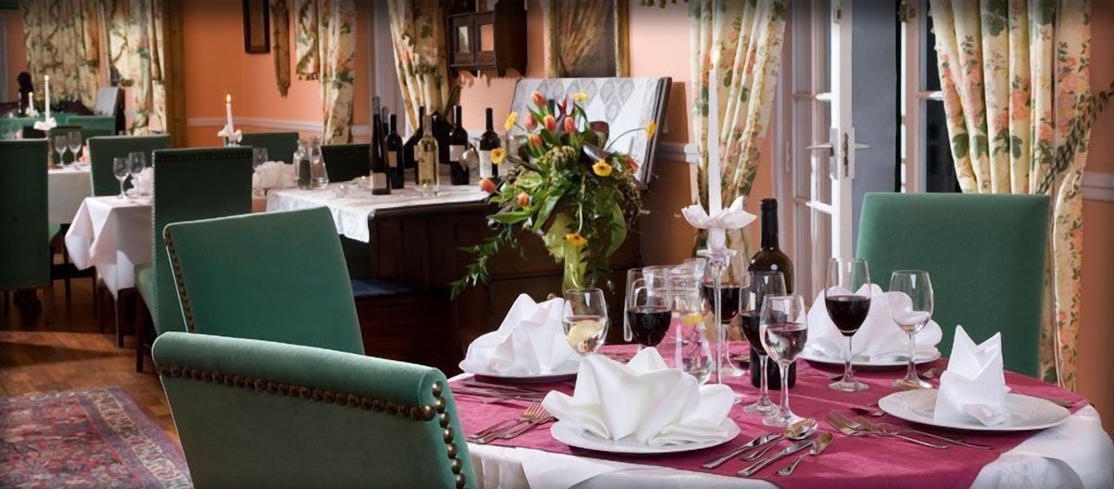Un restaurant où les tables sont dressées pour le service, avec des chaises vertes, des nappes blanches et des centres de table floraux.