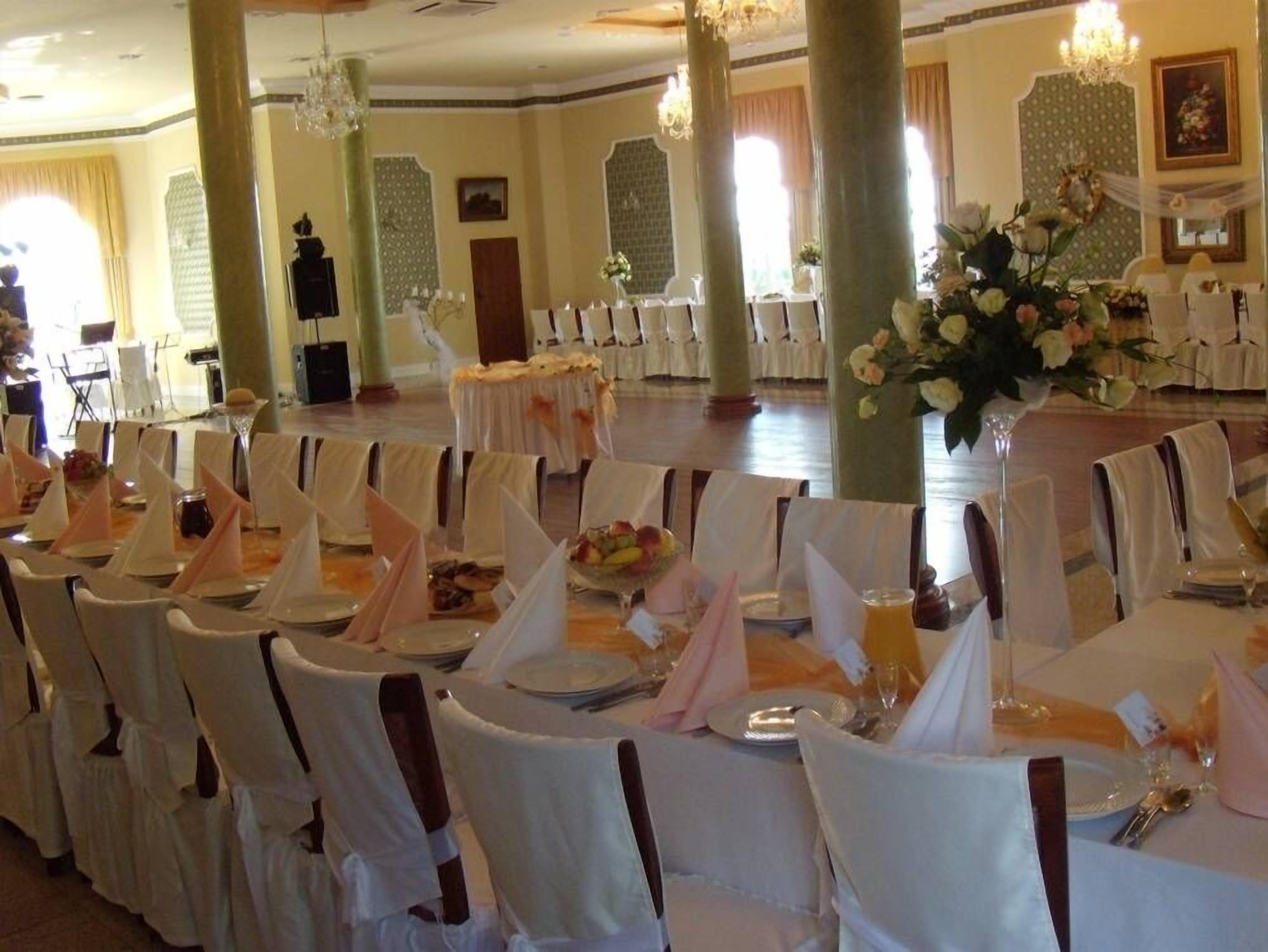 Ein Festsaal mit Tischen, die für eine festliche Veranstaltung gedeckt sind, verziert mit weißen Tischdecken und floralen Mittelpunkten.