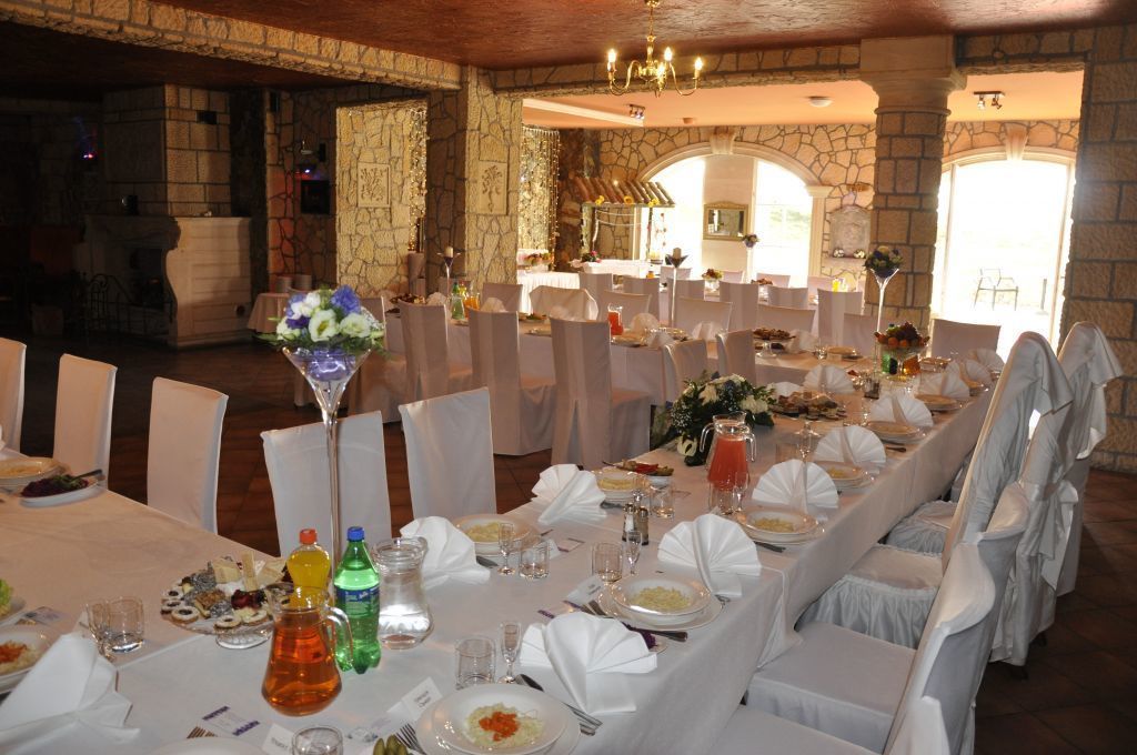 Een balzaal met meerdere ronde tafels gedekt voor een formeel evenement, stenen muren en een kroonluchter.