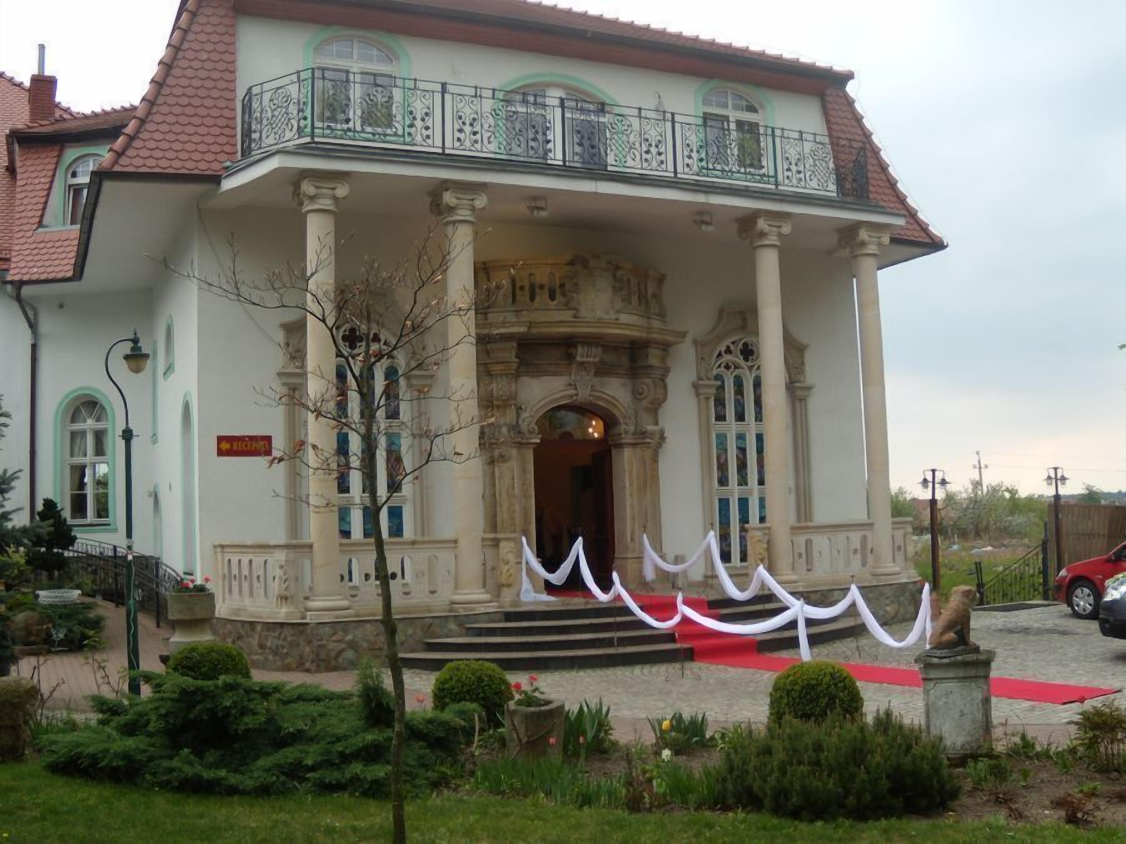Un edificio histórico con una entrada imponente, columnas ornamentadas y un balcón con barandillas decorativas.
