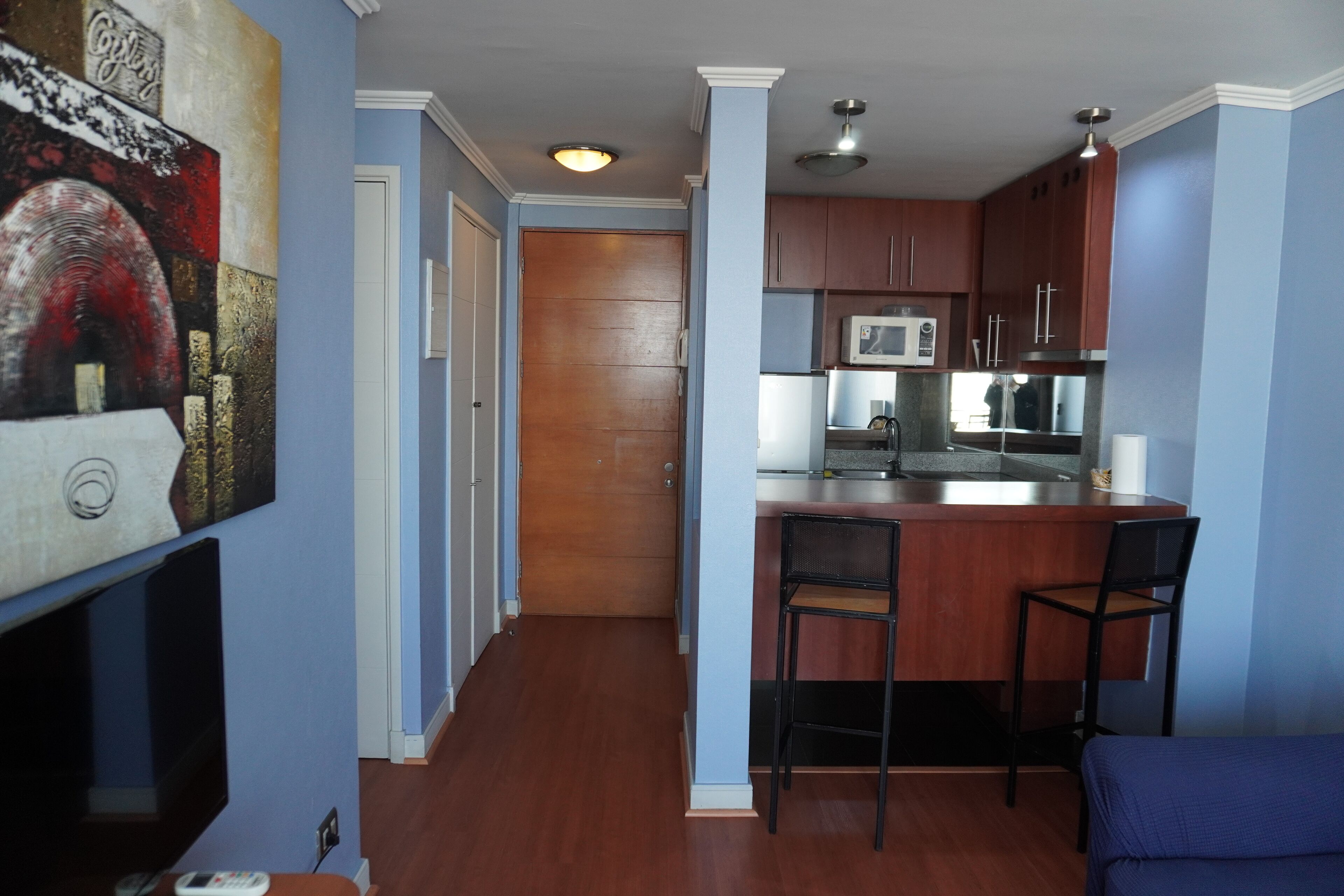 A kitchen with wooden cabinets, a microwave, and a bar area with two chairs.