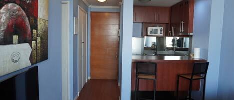 A kitchen with wooden cabinets, a microwave, and a bar area with two chairs.