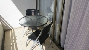 Een klein balkon met een glazen tafel, twee stoelen, een schuifpui en uitzicht op de omgeving.