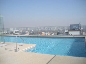 A rooftop pool with a city view, a glass railing, and a PAZ sign. - Departamentos Pontoni (Santiago)