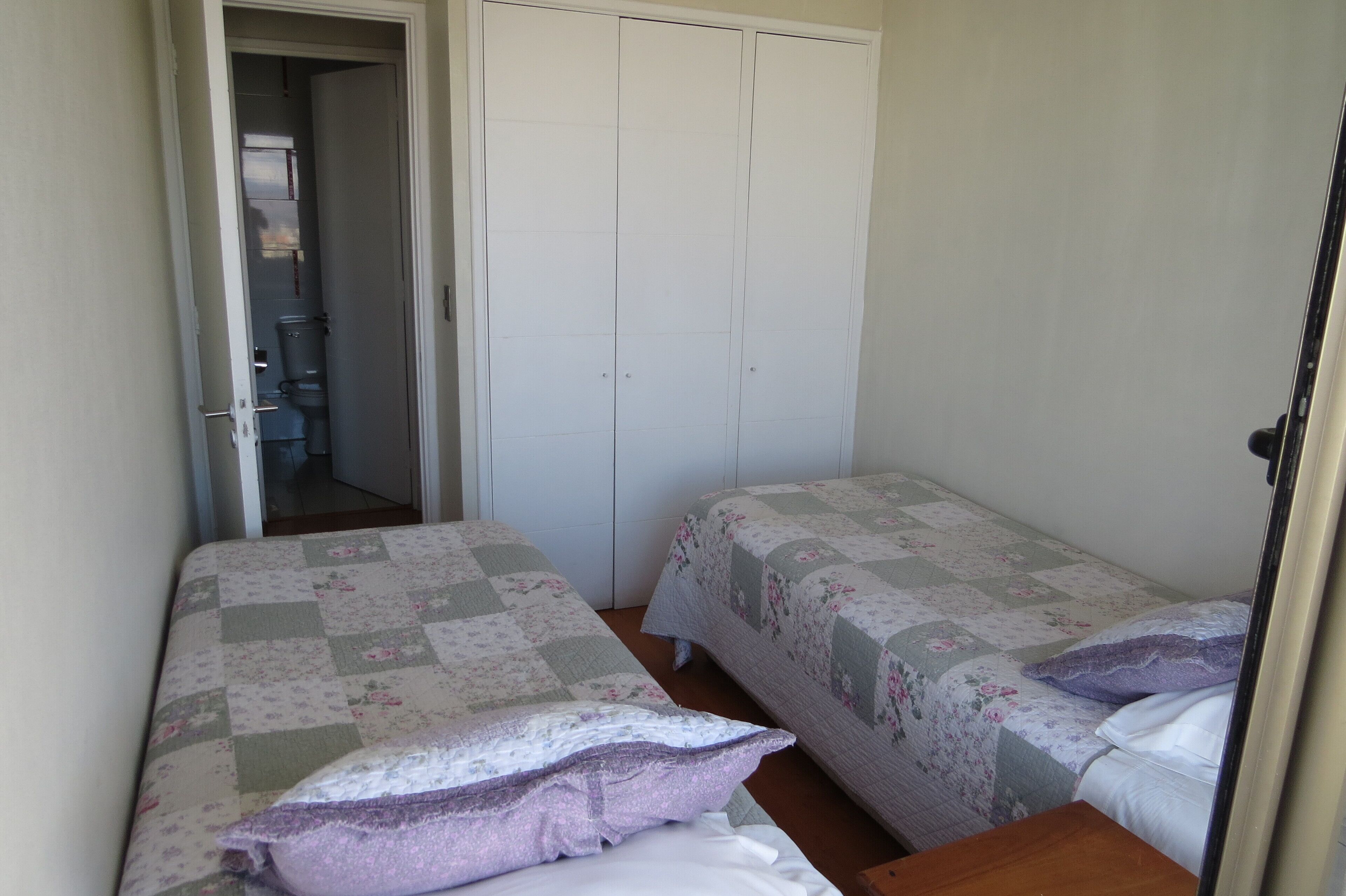 Un dormitorio con dos camas individuales, un armario y un baño visible a través de una puerta abierta.