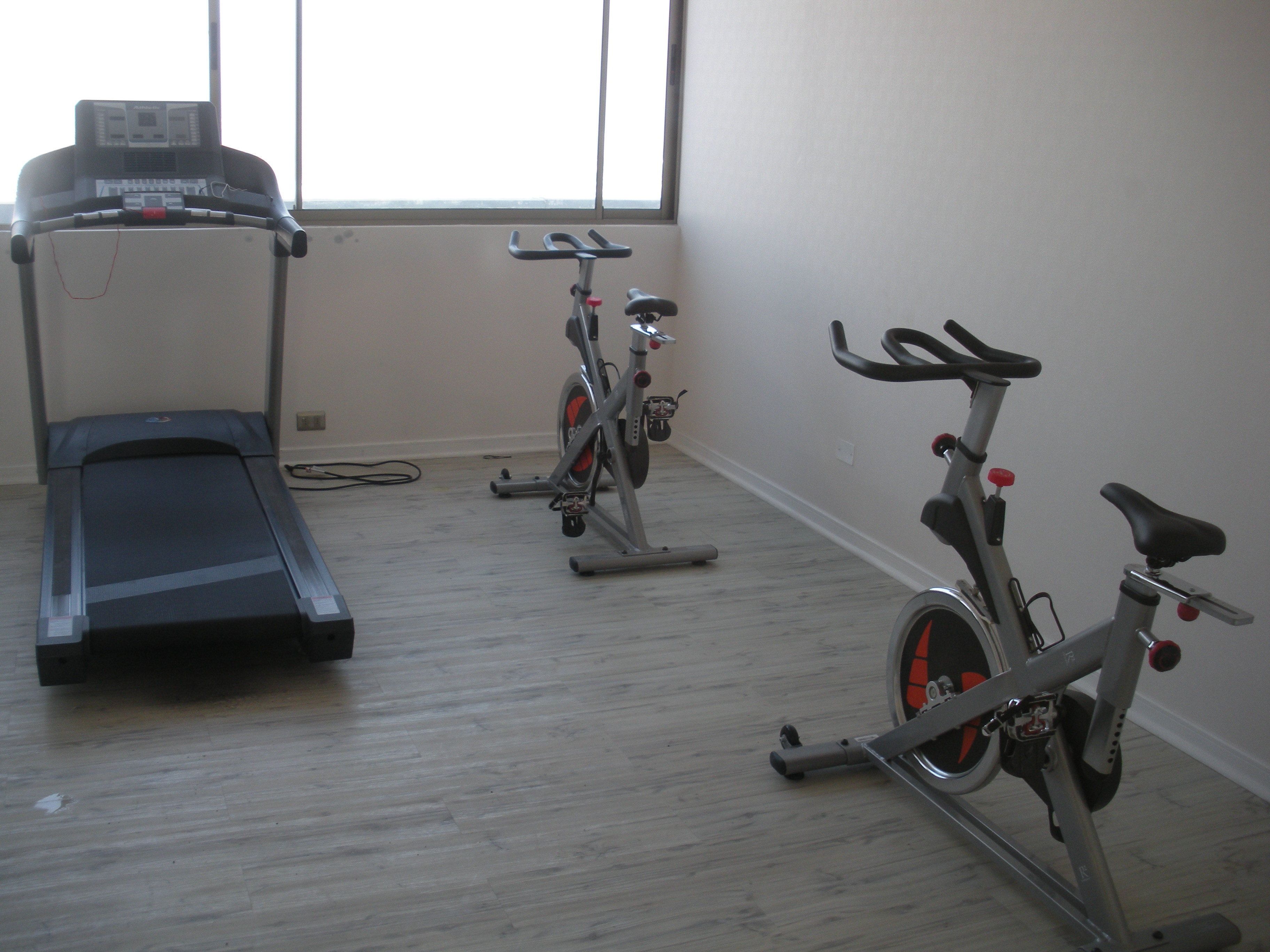 Uma academia em casa com esteira, bicicletas ergométricas e equipamentos de ginástica.