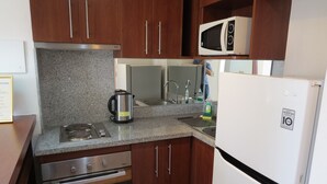 Een compacte keuken met granieten aanrechtbladen, een roestvrijstalen fornuis, een magnetron en een koelkast.