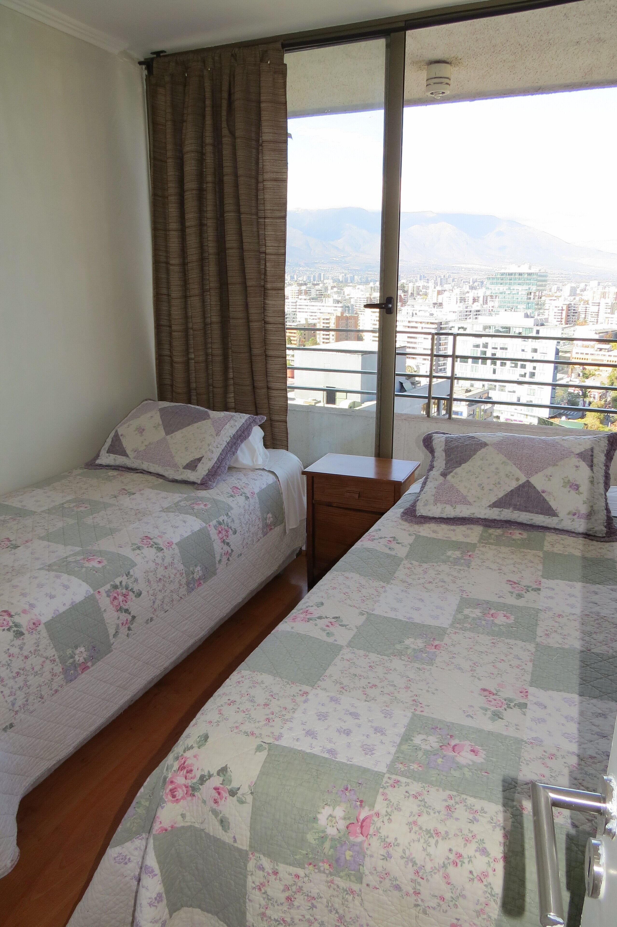Ein Schlafzimmer mit zwei Betten, einem Fenster mit Vorhängen und Blick auf die Stadt.