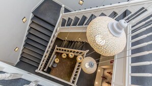 A modern staircase with a glass railing, a decorative chandelier, and a wooden interior.